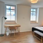 Schlafzimmer mit Bett, Schreibtisch und zwei Fenstern.