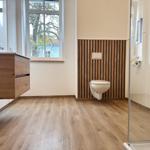 Badezimmer mit Holzboden, Toilette an Holzwand, Dusche und Waschtisch