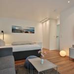 Schlafzimmer mit Bett, Sofa, Fernseher und Holzboden.