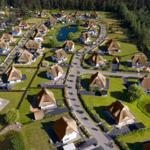 Luftbild von Ferienhäusern mit Strohdächern, Grünflächen und einem Teich.