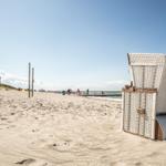 Weißer Strandkorb mit der Nummer 99 auf Sandstrand bei sonnigem Wetter.