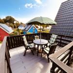 Terrasse mit Tisch, Stühlen und Sonnenschirm. Blick auf rote und blaue Häuser.