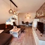 Wohn- und Essbereich mit Sofa, TV und Steinwand. Essplatz mit Tisch und Stühlen.