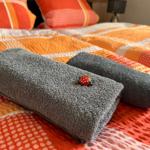 Zwei graue Handtücher liegen auf einem Bett mit bunten Kissen und Bettwäsche.