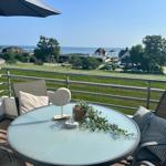 Terrasse mit Tisch und Stühlen. Blick auf Grünfläche und Meer.