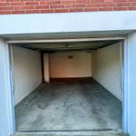 Garage mit Betonboden und weißen Wänden, rote Ziegelwand darüber.