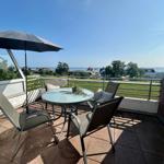 Terrasse mit Tisch, Stühlen und Sonnenschirm. Blick auf Grünfläche und Meer.