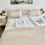 Doppelbett mit weißer Bettwäsche und hellen Kissen. An den Seiten Nachttische mit Lampen.