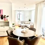 Essbereich mit runder Tisch und vier Stühlen. Wohnbereich mit Sofa und großen Fenstern.