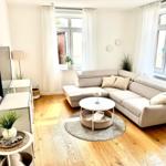 Wohnzimmer mit Ecksofa, runden Tisch und Holzboden.