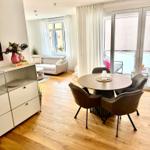 Ein Essbereich mit runden Tisch und Stühlen, daneben Wohnbereich mit Sofa und Balkon.