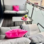 Terrasse mit Sofa, Sitzgruppe und Tisch. Pinker Kissen und Pflanze.
