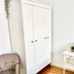 Weißer Schrank mit schwarzen Knöpfen, graue Sitzgelegenheit und runder Teppich.