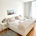 Ein Schlafzimmer mit weißem Bett, Holzboden und Fenster mit weißen Vorhängen.