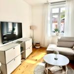 Wohnzimmer mit Sofa, TV und Fenster. Holzboden und runder Tisch.