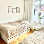 Zwei Betten mit Bezügen, Fenster mit Vorhängen und Bilder an der Wand.