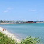 Strand mit Booten und klarem Wasser. Menschen spazieren entlang des Ufers.