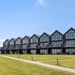 Reihe moderner Holzgebäude mit Balkonen und großen Fenstern auf grünem Rasen.