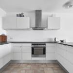 Moderne Küche mit weißen Schränken, Edelstahlherd und dunklem Arbeitsplatz.