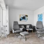 Wohnzimmer mit grauen Sesseln, Sofa und abstrakten Bildern an den Wänden.