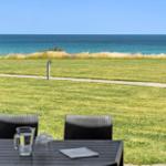 Terrasse mit Tisch und Stühlen. Blick auf Grasfläche und Meer.