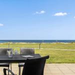 Terrasse mit Tisch und Stühlen, Blick auf Grasfläche und Meer mit Booten.