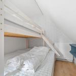 Doppelstockbett mit Matratzen und weißer Bettwäsche in einem Dachzimmer mit Holzboden und Regal.