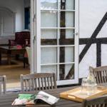 Terrasse mit Tisch und Stühlen. Durch Glastüren ist Wohnzimmer mit Möbeln sichtbar.