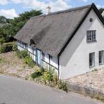Traditionelles Haus mit Strohdach und weißer Fassade. Garten und Steinweg sichtbar.