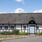 Ein weißes Fachwerkhaus mit strohgedecktem Dach und blauer Tür.