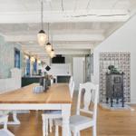 Esszimmer mit Holztisch, weißen Stühlen und Kachelofen an der Wand.