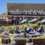 Außenbereich mit Tischen und Stühlen vor einem Restaurant mit Schild.