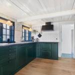 Küche mit grünen Schränken, Holzboden und Fenstern mit Blumenpapier.