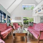 Wohnzimmer mit rosa Polstersofas, Glas-Tisch und Holzboden. Fenster mit floraler Tapete.