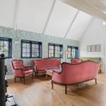 Wohnzimmer mit rosa Sitzmöbeln, floraler Tapete und Holzboden. Durchgang zur Terrasse.