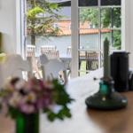 Ein Essbereich mit Tisch und Stühlen. Durch Fenster ist ein Garten mit Tisch und Stühlen sichtbar.