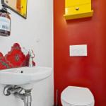 Bad mit Waschbecken, Toilette und gelbem Schrank an roter Wand.