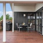 Terrasse mit Tisch, Stühlen und Grill. Holzdecke und Glaswände.