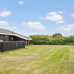 Schwarzes Haus mit Garten und Zaun unter blauem Himmel.