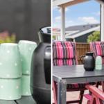 Terrasse mit Tisch, Stühlen und Tassen. Hintergrund: Haus und Himmel.