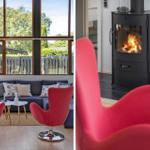 Ein Wohnzimmer mit roten Sesseln und Kamin. Große Fenster bieten Blick auf Garten.