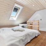 Schlafzimmer mit Dachschrägen, Holzwand und Dachfenster. Bett mit Holzgestell und weißer Bettwäsche.