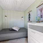 Ein Schlafzimmer mit grauem Bett, weißem Schrank und Streifenwand.