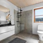 Badezimmer mit Dusche, Waschbecken und Toilette. Holzdecke und Fenster mit Holzrahmen.