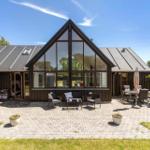 Modernes Haus mit großem Glasbereich und gepflastertem Hof mit Gartenmöbeln.