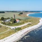 Haus mit Leuchtturm an Küste, Strand und Felder im Hintergrund.