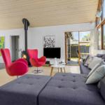 Wohnzimmer mit grauem Sofa, roten Stühlen und Kamin. Große Fenster und Türen zu Garten.