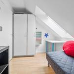 Schlafzimmer mit Dachschräge, Bett, Schrank und Schreibtisch.