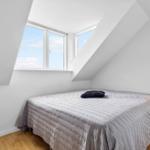 Schlafzimmer mit Dachschrägen, großem Fenster und zwei Nachttischen mit Lampen.