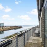 Terrasse mit Blick auf Hafen und Meer. Autos parken entlang des Ufers.